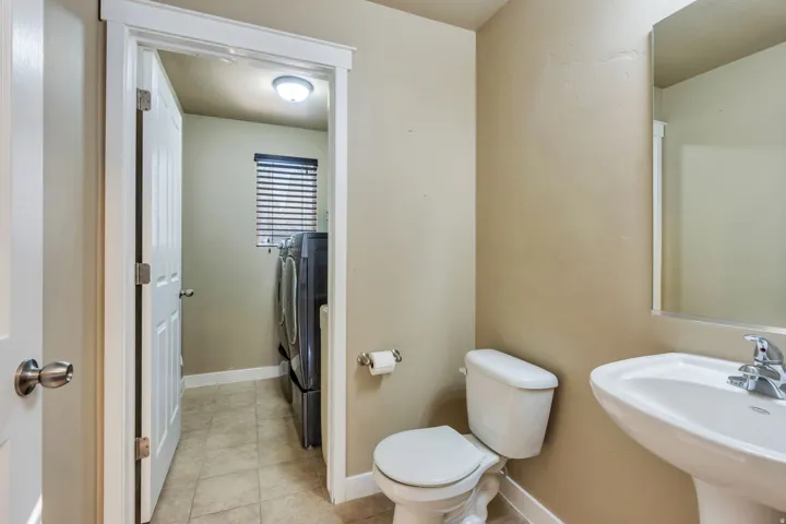 Pedestal sink with chrome faucet, toilet, wall-mounted mirror, and tile flooring