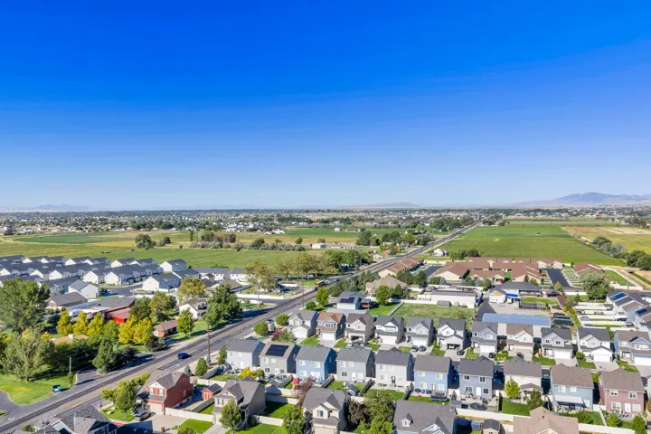 Residential development with a clear sky backdrop, surrounded by expansive green fields and distant mountains