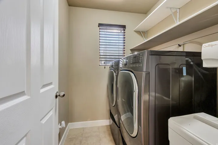 Utility area with tile flooring, built-in shelving, and a window with blinds