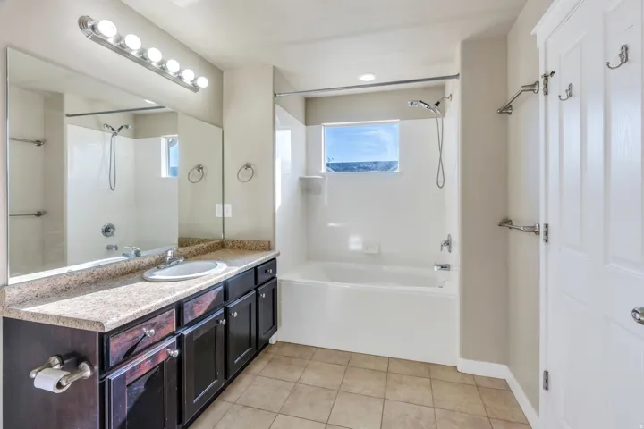 Full-width vanity mirror, a single basin sink, a built-in bathtub with shower, and tile flooring