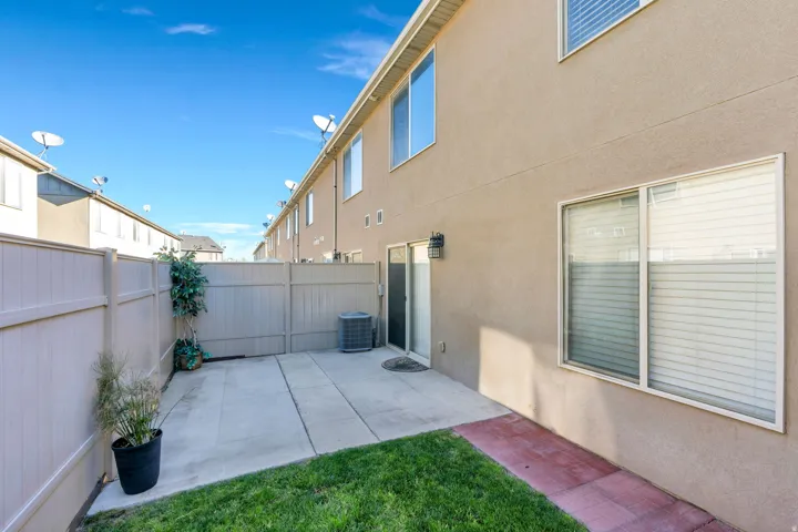 Private fenced patio with concrete and grass areas, featuring a stucco exterior with multiple windows and a sliding glass door