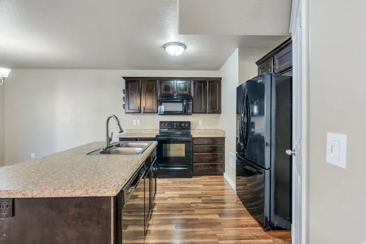 Kitchen featuring wood-finish flooring, dark wood cabinetry, black appliances, and speckled countertops