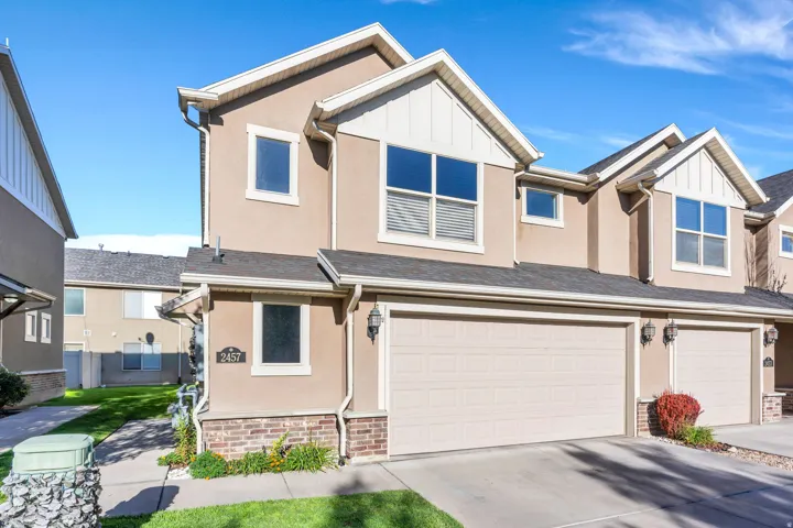 Stucco exterior with gabled dormers, an attached two-car garage, brick accents, and exterior lighting fixtures