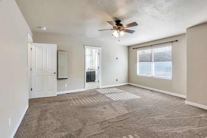 Spacious room featuring neutral carpet, a large window with blinds, and a ceiling fan