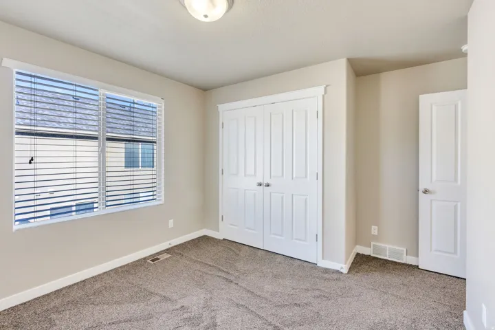 Neutral wall paint, carpet flooring, a multi-pane window with blinds, and white panel doors