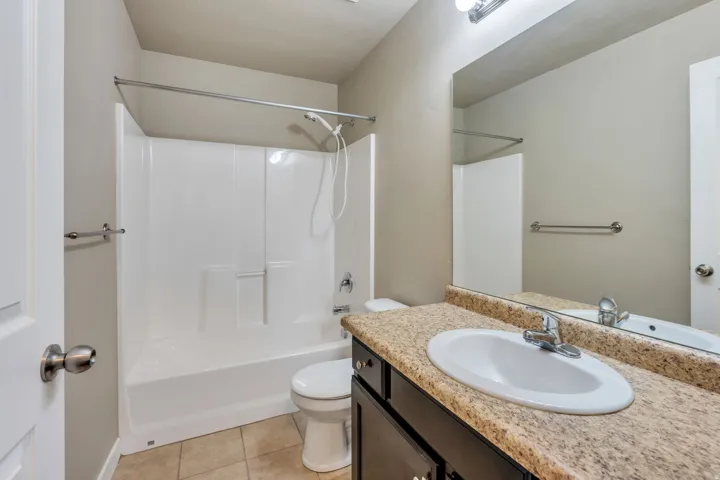 Bathroom featuring a shower/tub combination, single vanity with an integrated sink, broad wall mirror, and tile flooring