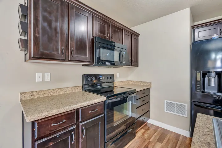 Dark wood-finish cabinetry, black appliance suite, speckled countertops, wood-finish flooring, and built-in microwave