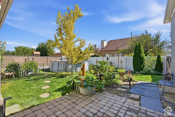 Paver patio with a stone path, grass lawn, white privacy fencing, and mature trees