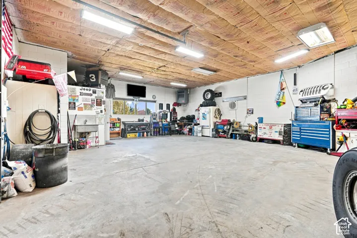 Spacious garage with exposed insulation ceiling, concrete flooring, and multiple fluorescent light fixtures