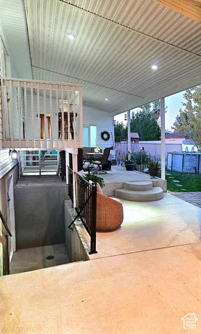 Covered patio with integrated recessed lighting, concrete steps, and a black wrought iron railing