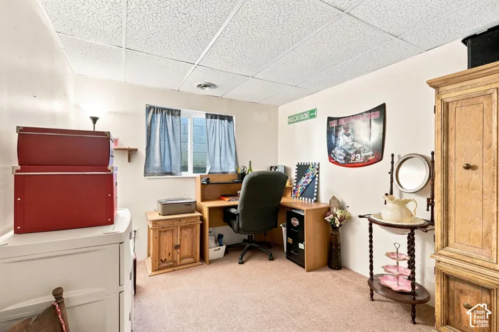 Finished Basement Recreation Room with Carpeted Flooring, Drop Ceiling, Large Windows with Blue Curtains, Wood Cabinetry, Built-In Shelving, and Ample Space for Home Office or Studio Use