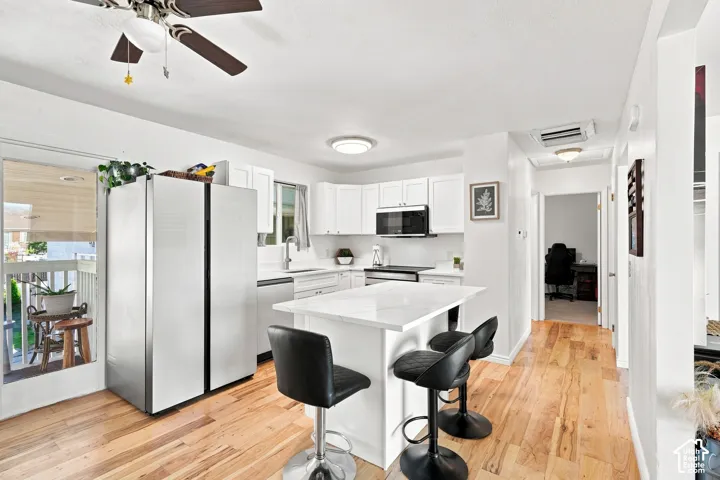 Kitchen with white cabinetry, stainless steel appliances, and wood-finish flooring