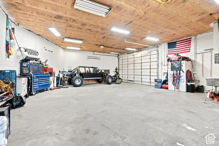 Spacious garage featuring concrete flooring, an overhead garage door, built-in shelving, and exposed ceiling insulation