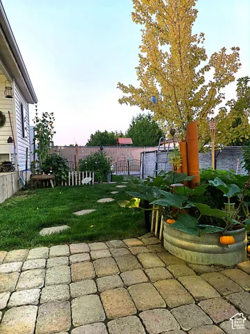 Paver patio leading to a manicured lawn, established landscaping, stepping stones, and a privacy fence