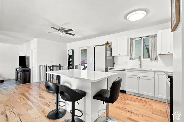 Kitchen featuring white cabinetry, light-toned countertops, a stainless steel sink with a gooseneck faucet, and wood-finish flooring