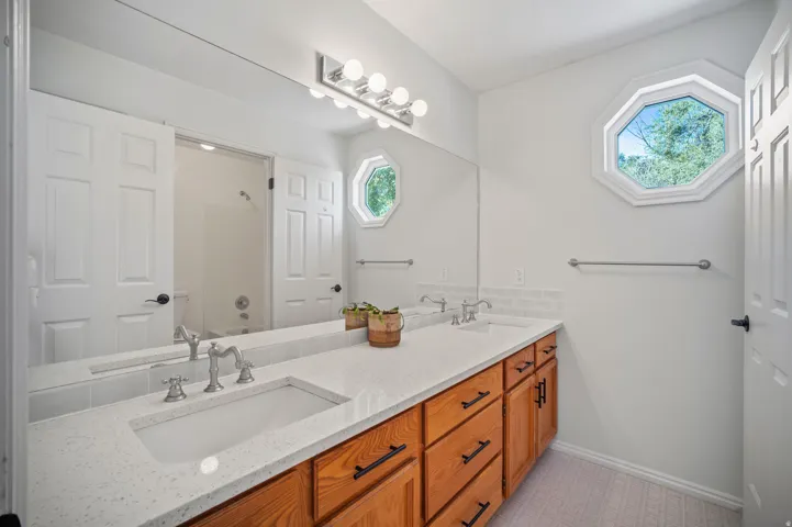 Dual vanity with integrated sinks and chrome fixtures, wood-finish cabinetry with black hardware, and a full-width mirror