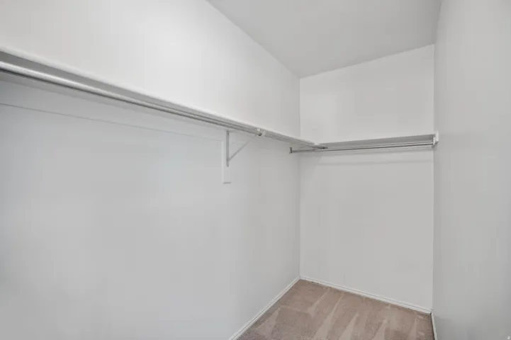 Recessed walk-in closet with carpet flooring, white walls, and built-in shelving with hanging rods