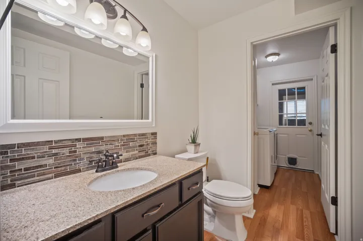 Vanity with granite-style countertop, undermount sink, and mosaic tile backsplash