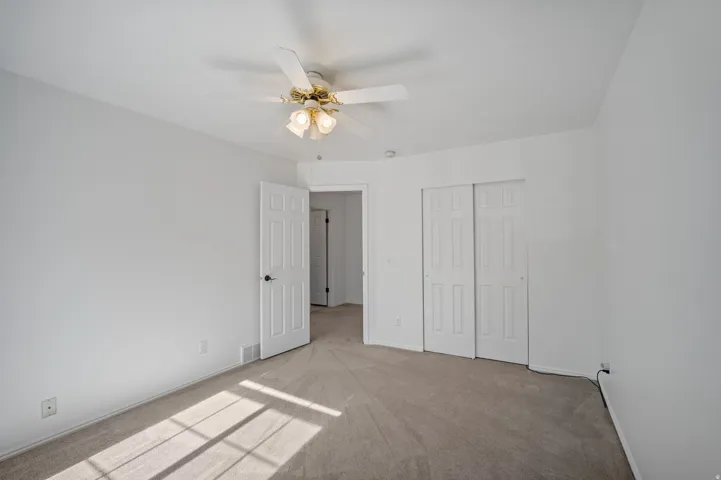 Carpeted room featuring a ceiling fan with integrated lighting, a paneled door, and sliding closet doors