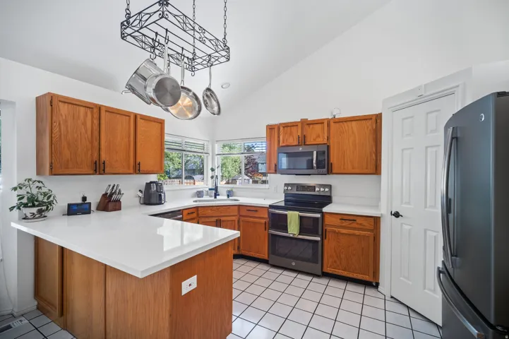 Vaulted ceiling kitchen featuring wood cabinetry, white countertops, tile flooring, and stainless steel appliances