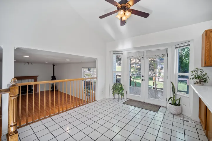 Vaulted ceiling with a ceiling fan, white tile flooring, double French doors, wood railing, and wood-finish flooring in the lower level