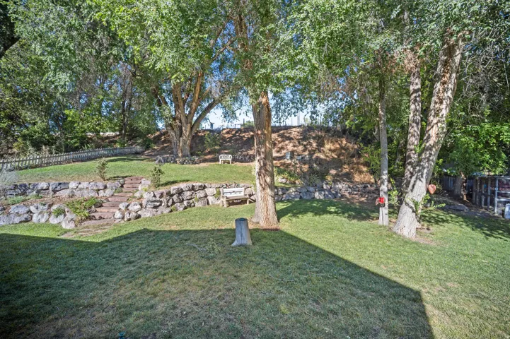 Expansive terraced yard with mature trees, manicured lawn, and stone retaining walls