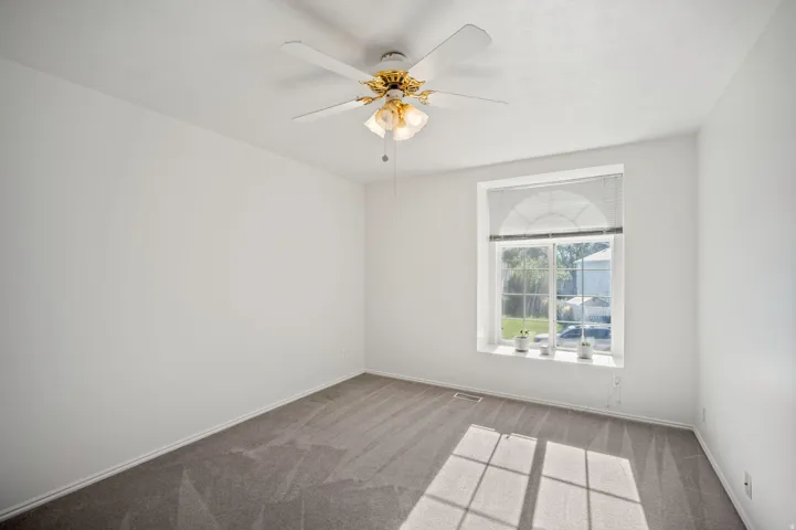 Arched window with blinds, ceiling fan with integrated lighting, and neutral carpeting