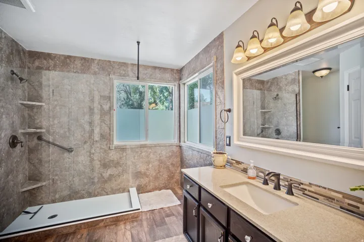 Walk-in shower with built-in shelving, wood-finish flooring, dual windows, vanity with integrated sink, and bronze fixtures