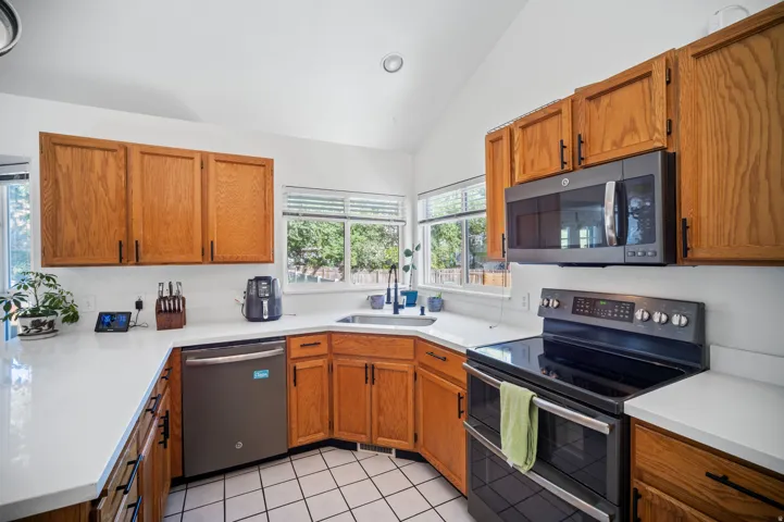 Kitchen featuring wood cabinetry, white countertops, stainless steel dishwasher, black electric range, and an over-the-range microwave