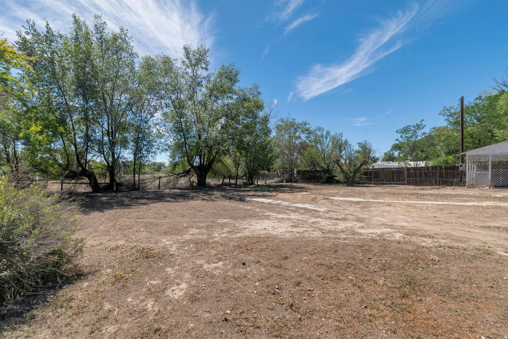 Expansive land with mature trees, perimeter fencing, and a detached structure