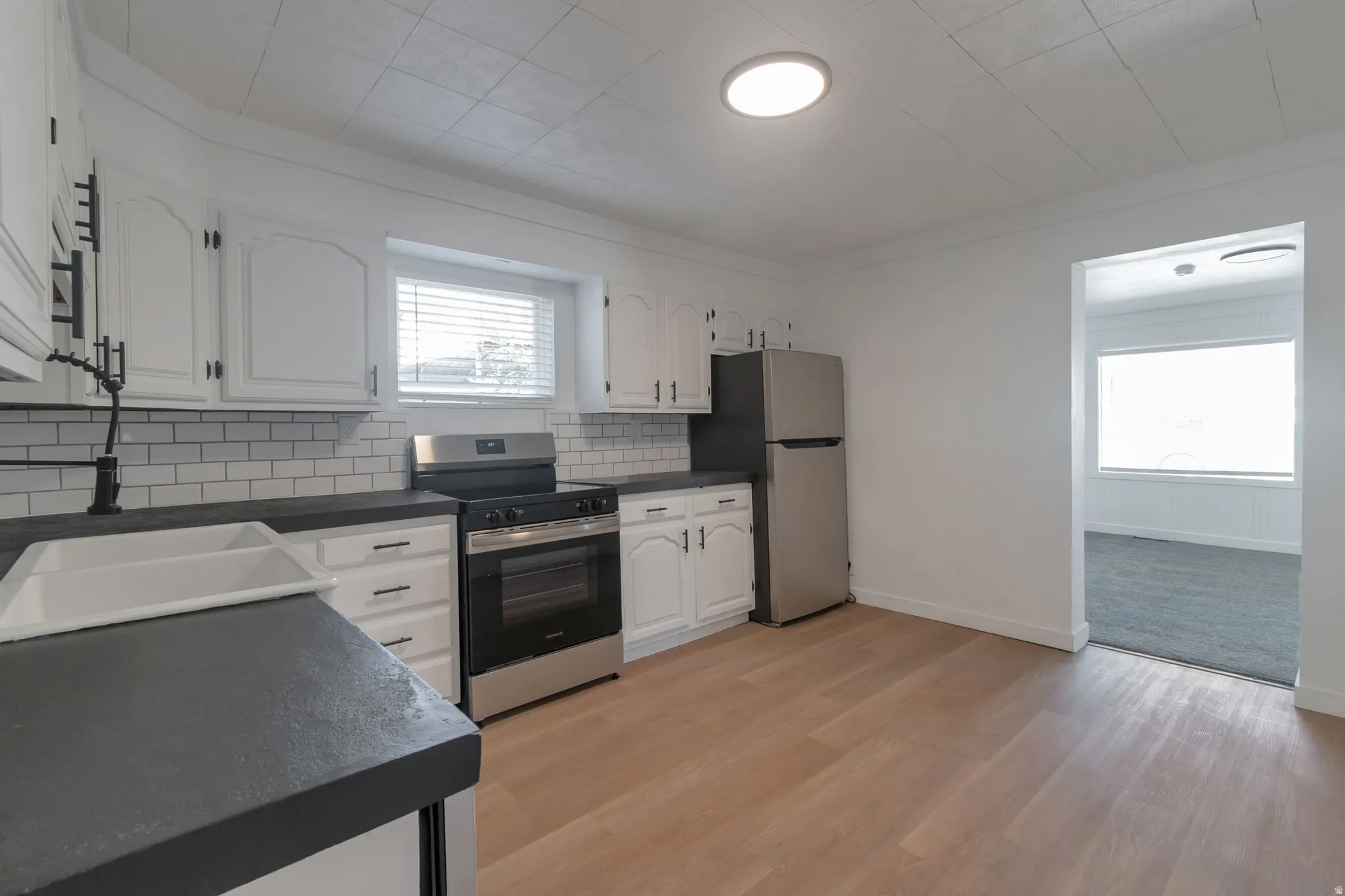 Kitchen featuring wood-finish flooring, white cabinetry, dark countertops, a white subway tile backsplash, and stainless steel appliances