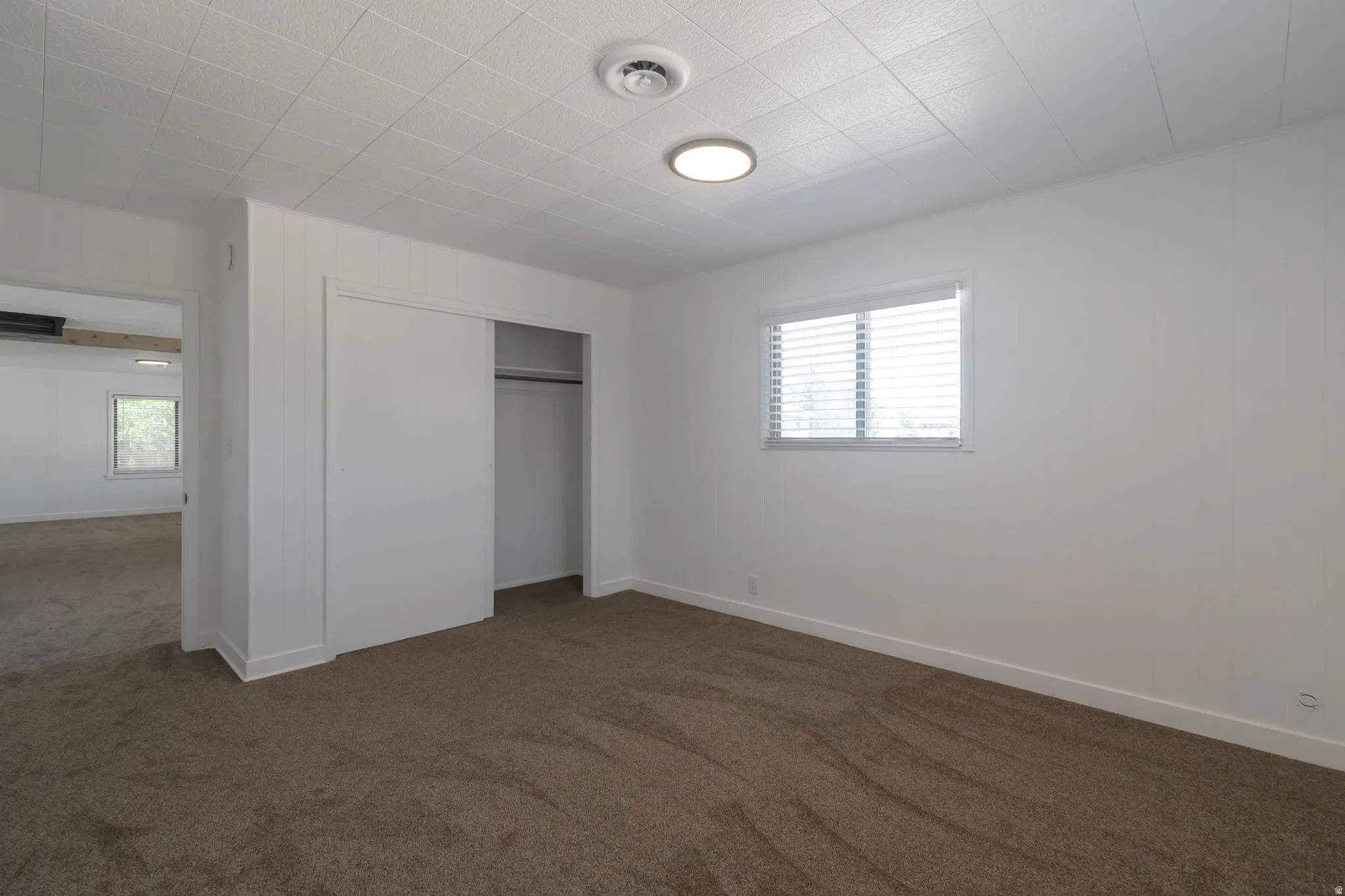 Wall-to-wall carpet flooring with white baseboards, a window with blinds, and a built-in closet with sliding doors