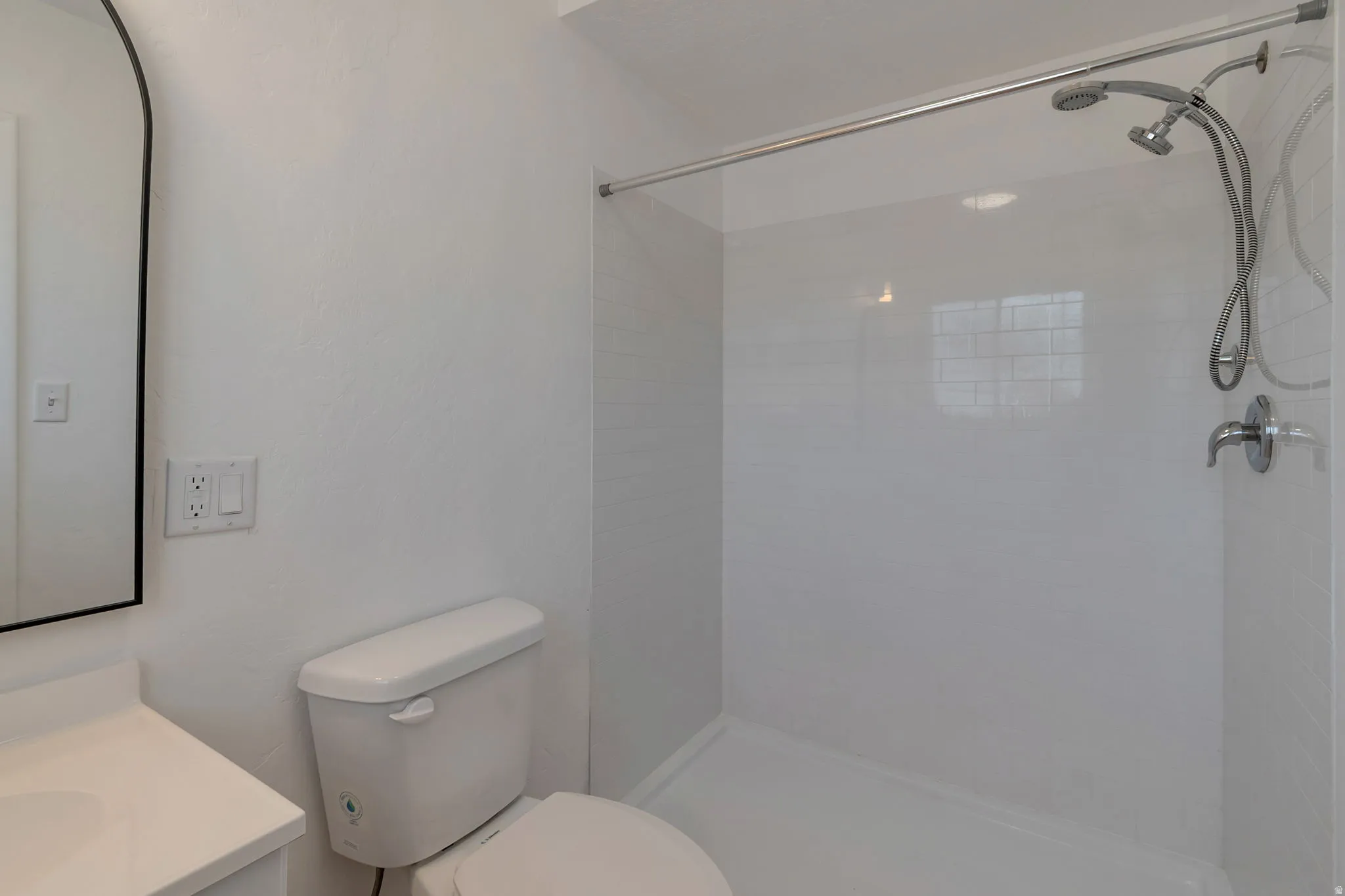 White vanity with an integrated sink, black-framed arched mirror, and a walk-in shower with white subway tile