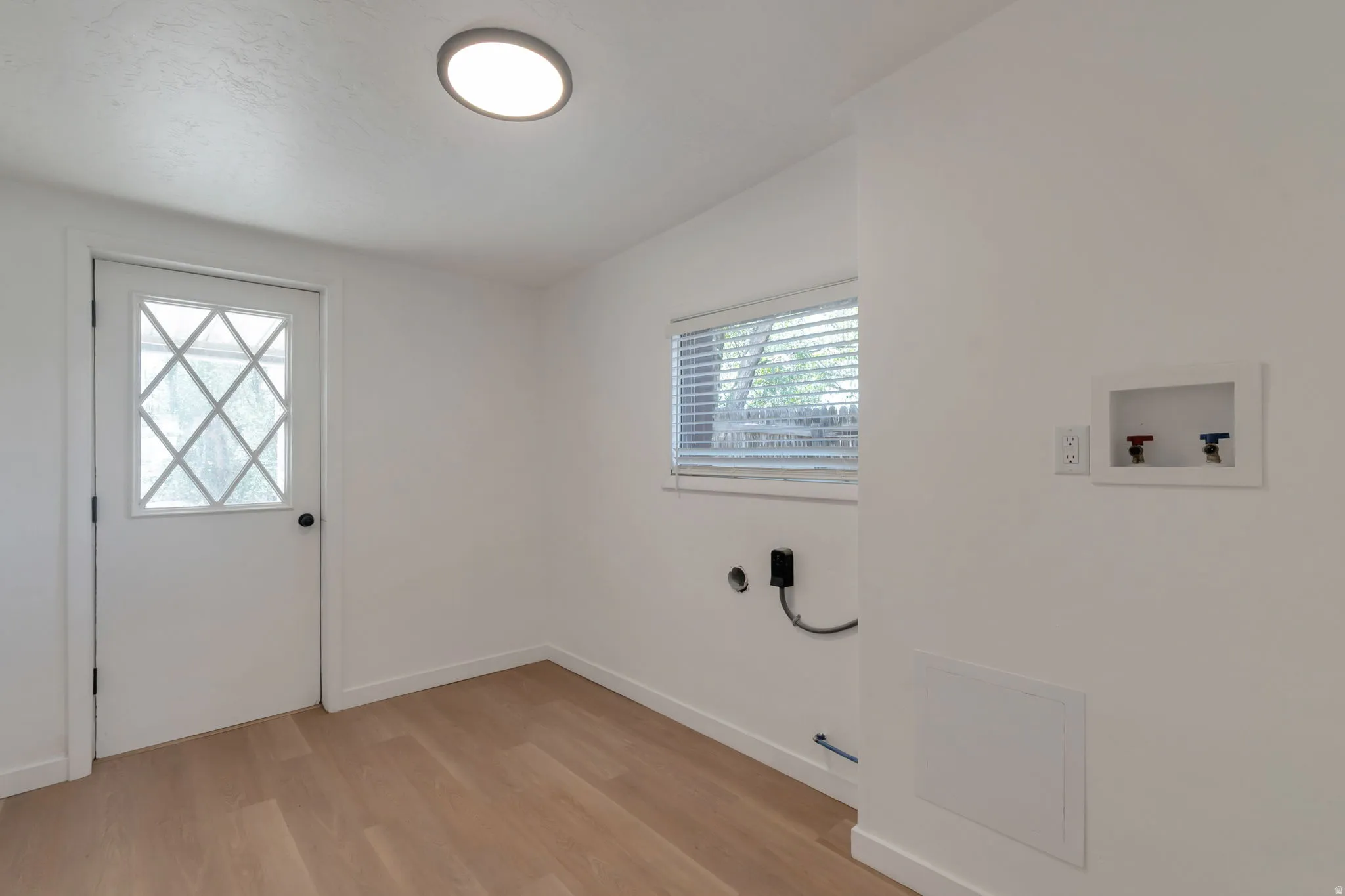 Laundry area featuring wood-finish flooring, a contemporary flush-mount ceiling light, a window with blinds, and appliance connections