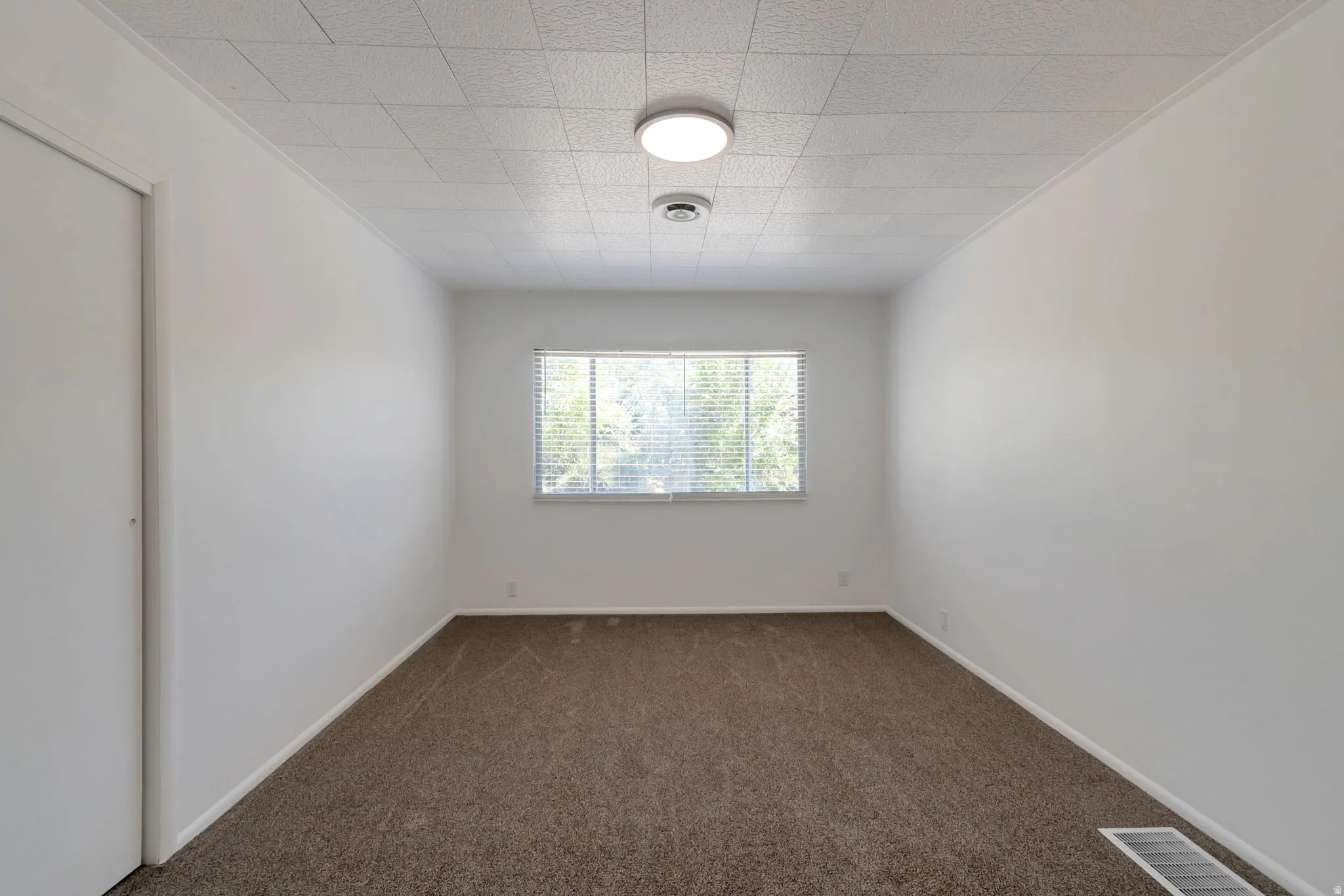Neutral wall finishes, recessed window, wall-to-wall carpeting, acoustic panel ceiling, and flush mount lighting