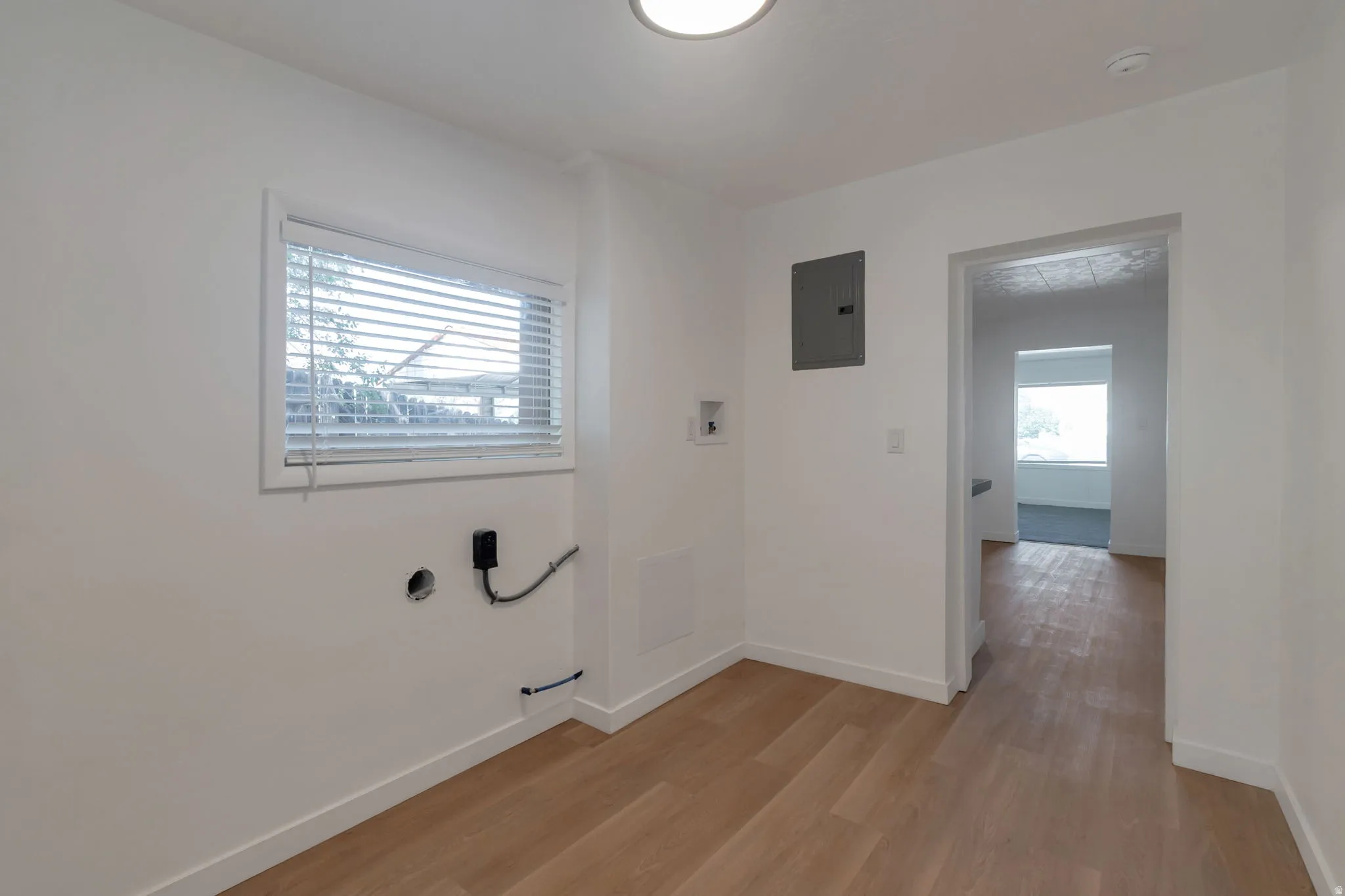 Light wood-finish flooring with white baseboards, window with blinds, and ceiling-mounted lighting fixture