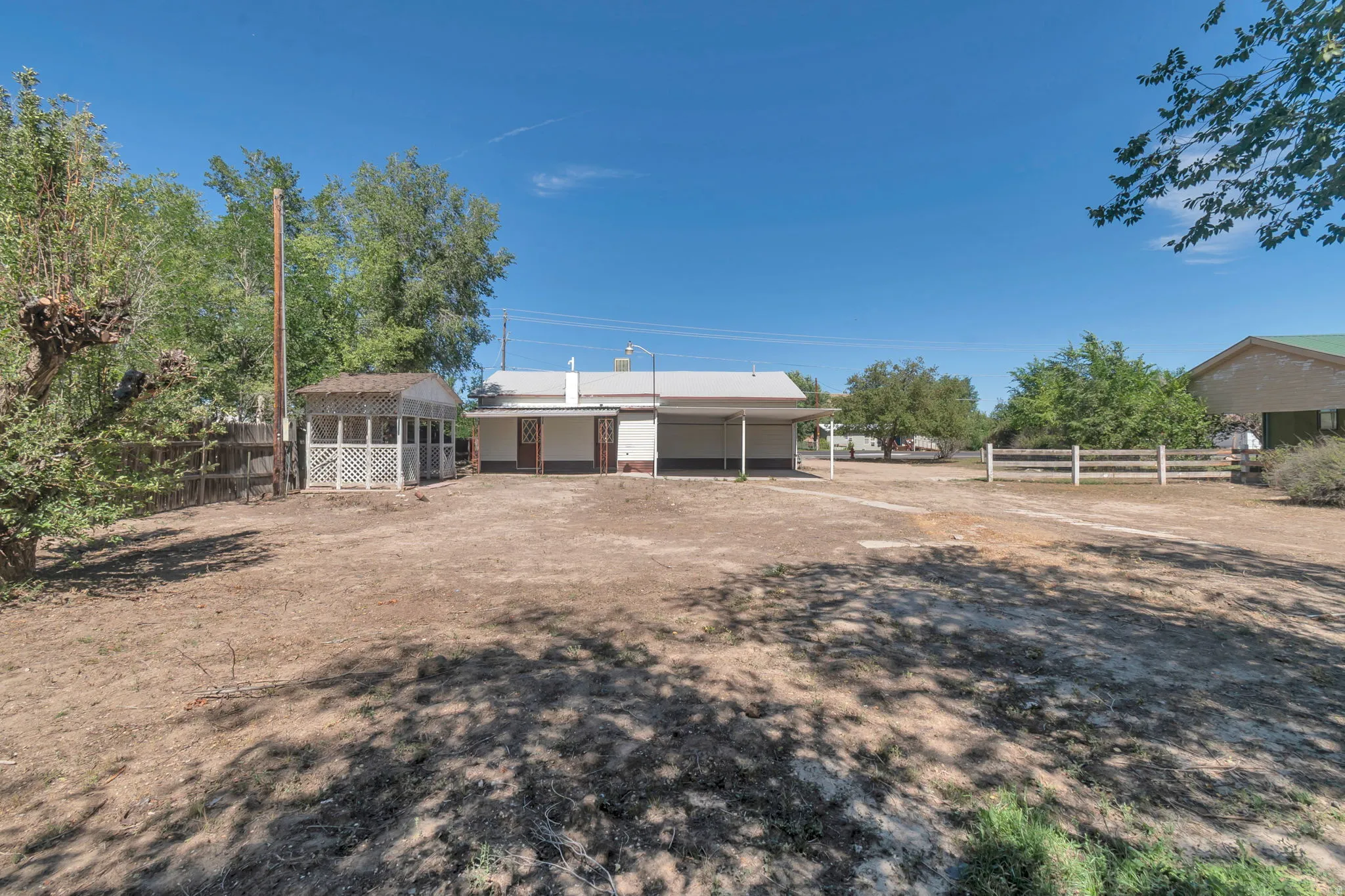 Expansive outdoor space featuring a covered porch, white lattice gazebo, and a multi-rail fence