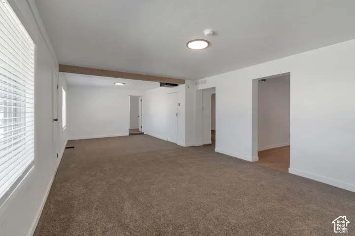 Expansive room featuring neutral-toned carpeting, white painted walls, and multiple window openings with blinds