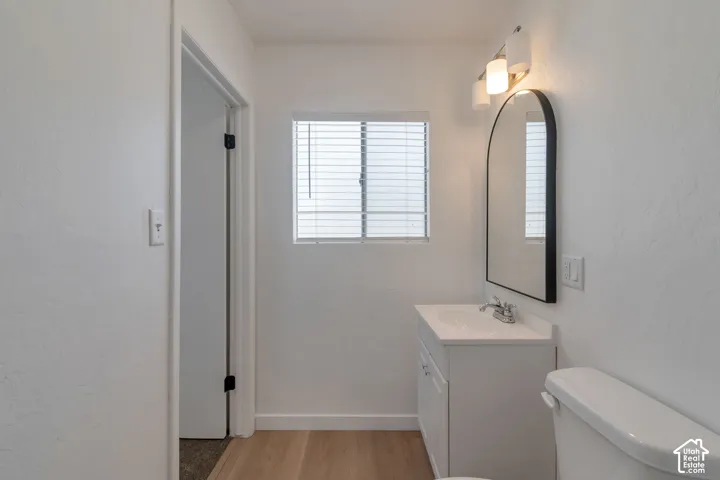 White vanity with an integrated sink, arched mirror, three-light vanity fixture, and wood-finish flooring