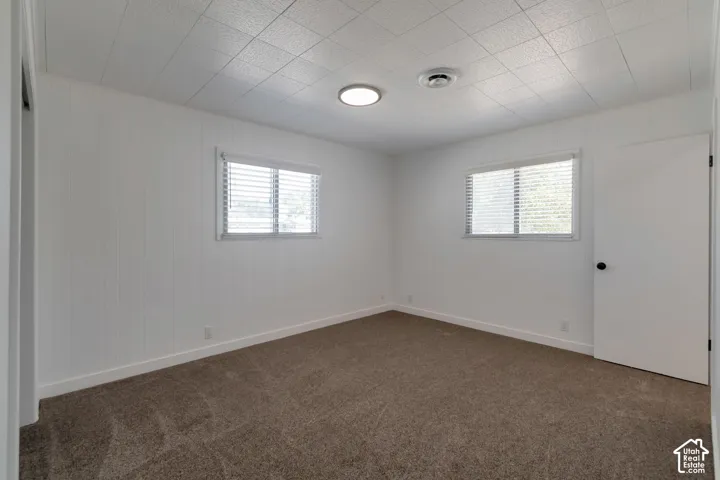 Neutral-toned carpet flooring, white paneled walls, and two windows with blinds
