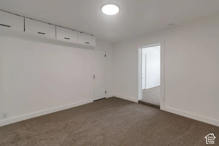 White walls with built-in overhead cabinetry featuring dark hardware, a flush-mount ceiling light, and brown carpeting