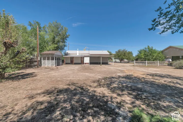 Expansive outdoor space featuring a covered porch, white lattice gazebo, and a multi-rail fence