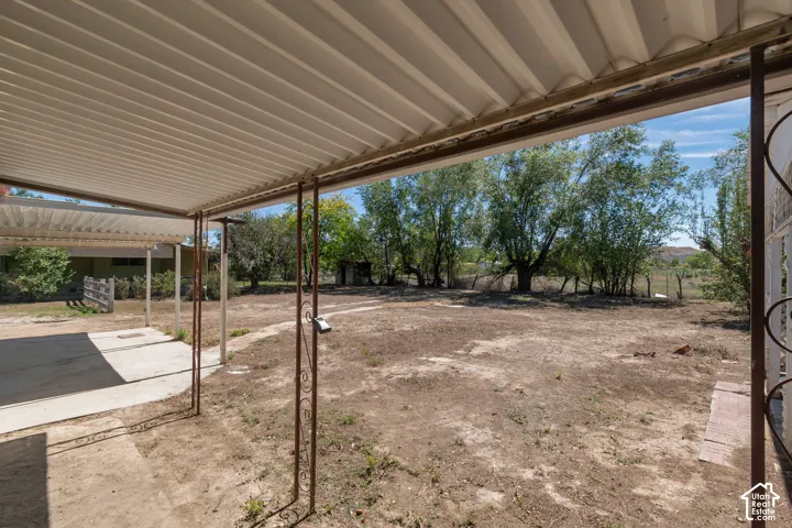Expansive outdoor area featuring a covered patio with corrugated metal roof, concrete slab, and wrought iron supports