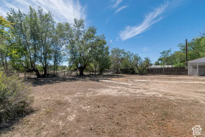 Expansive land with mature trees, perimeter fencing, and a detached structure