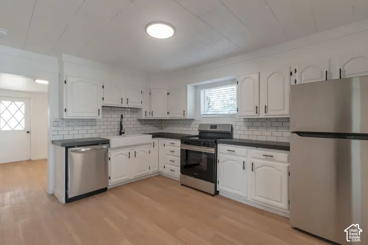 Kitchen featuring wood-finish flooring, white cabinetry, dark countertops, a farmhouse sink, and stainless steel appliances