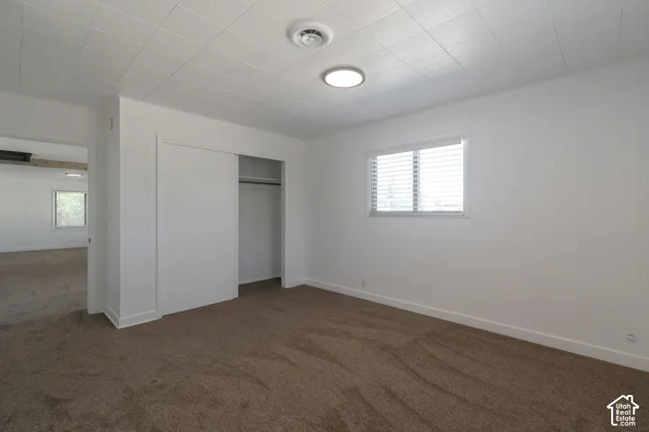 Wall-to-wall carpet flooring with white baseboards, a window with blinds, and a built-in closet with sliding doors