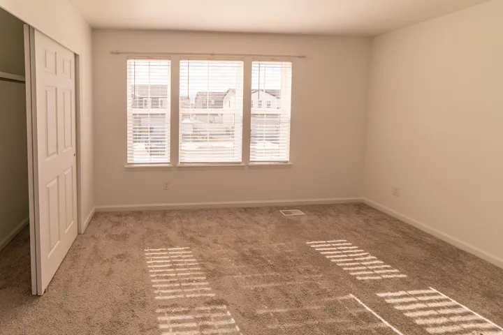 Neutral tone carpeting, three-panel window with white blinds, and white bi-fold closet doors