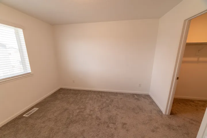 Carpeted room with a window featuring horizontal blinds, white walls, and an open closet with shelving