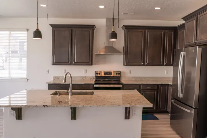 Kitchen featuring an island with a stainless steel sink, dark wood-finish cabinetry, stainless steel appliances, and light-toned granite countertops