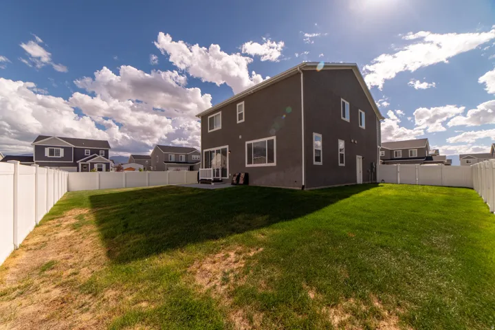 Expansive backyard featuring a manicured lawn, full white vinyl fencing, and a concrete patio